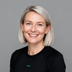 Smiling woman with short blonde hair wearing a black shirt against a gray background.
